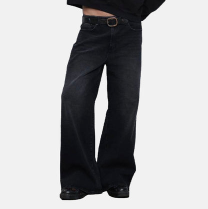 Person wearing black wide-leg jeans standing in front of a white shutter.